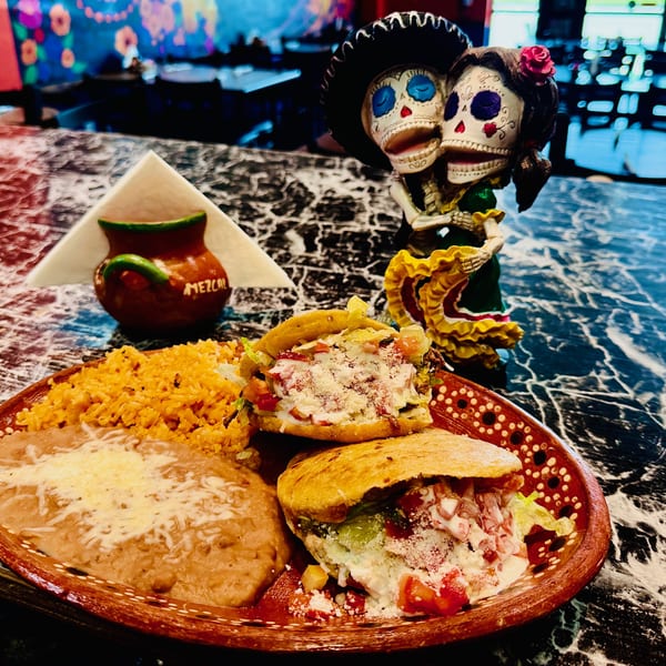 A Mexican dish with two gorditas, rice, and refried beans, next to a Day of the Dead figurine.