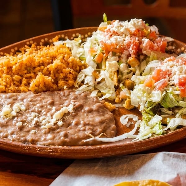 A platter with Mexican rice, refried beans, and two sopes topped with lettuce, tomato, and cheese.